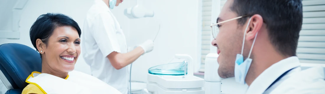 Dentist Feeding Hills MA Dental Crowns Focused a woman is seated in the dentists chair and is conversing with her dental hygienist